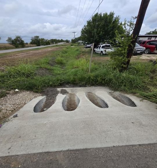 New concrete storm drain outlets under a driveway beside the road.